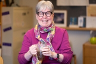 A smiling woman with gray hair and black glasses holding a large cup of tea